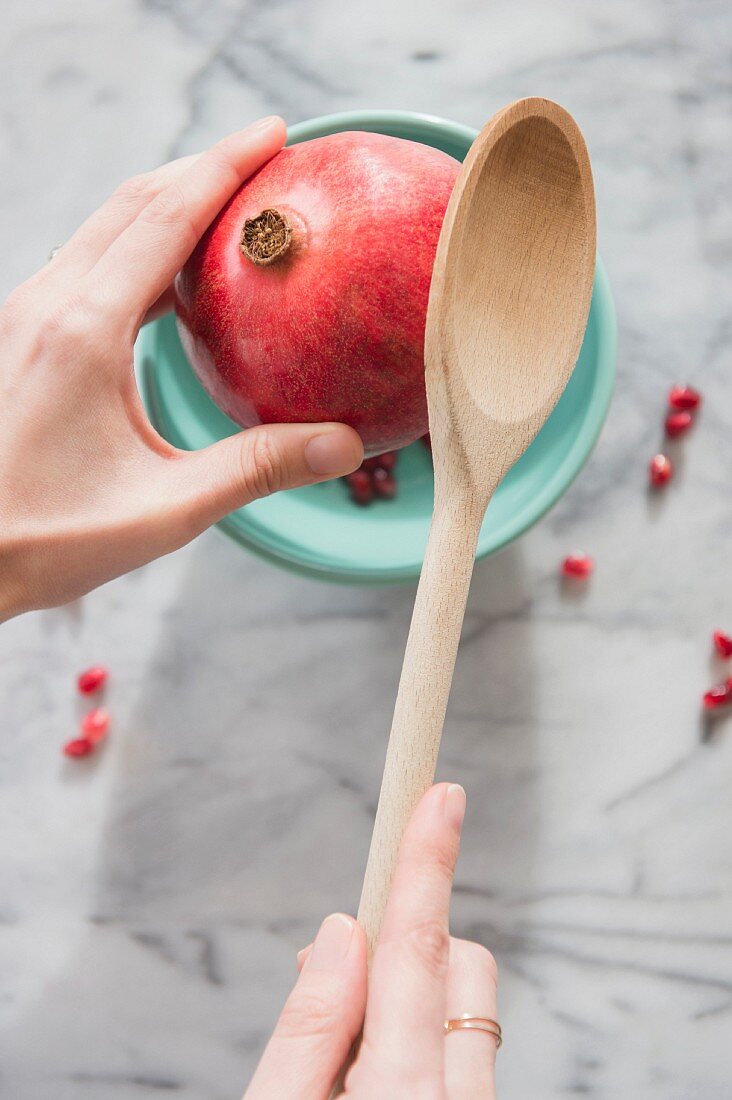 A pomegranate being opened with a wooden spoon