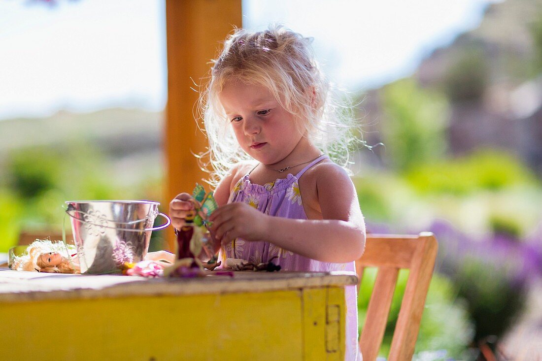 Kleines Mädchen spielt mit Puppen am Tisch auf der Terrasse