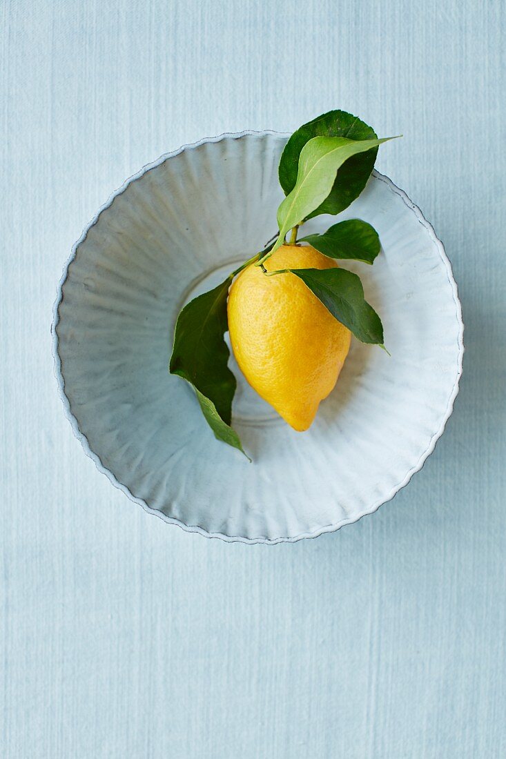 A lemon with leaves on a ceramic plate