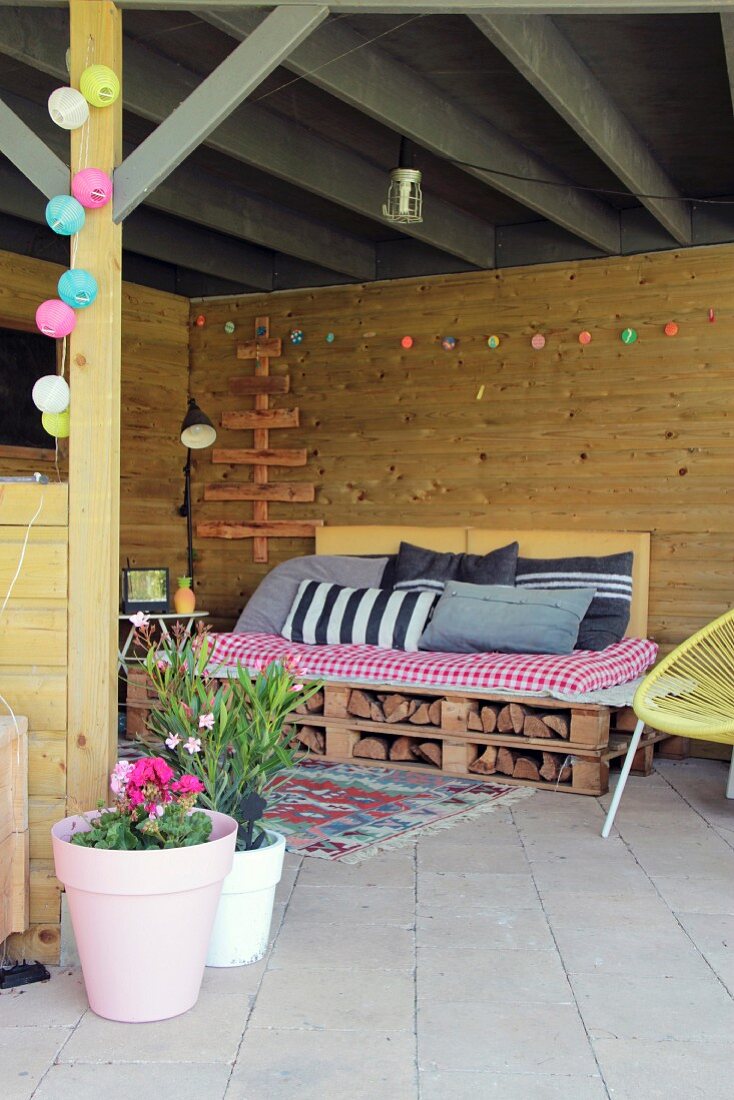 Gemütlicher, überdachter Terrassenplatz mit DIY-Palettencouch, Kissen und bunter Lichterkette