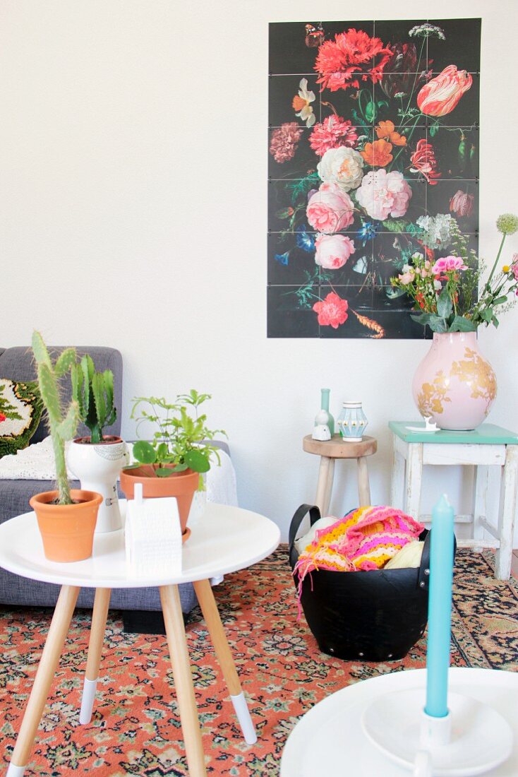 Beistelltisch mit Zimmerpflanzen vor Tasche mit Häkelarbeit, Vintage-Hocker mit Vase und buntem Blumenbild