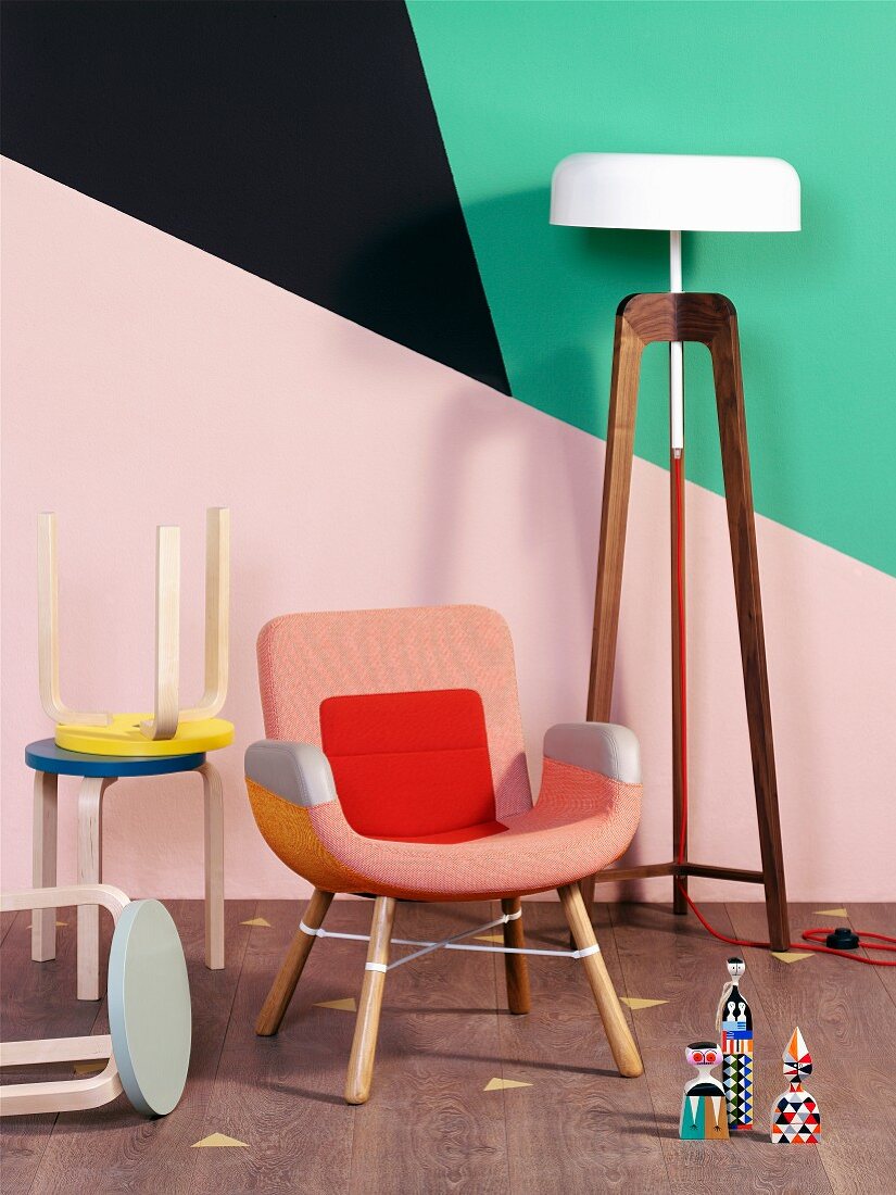 Hocker Sammlung und Sessel neben Stehleuchte vor Wand mit geometrischen Farbflächen