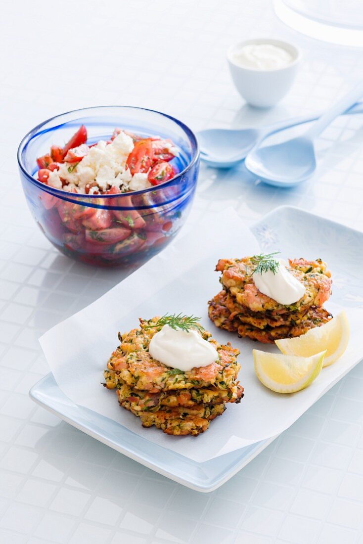 Courgette and salmon fritters with crème fraîche and dill served with a tomato and feta cheese salad