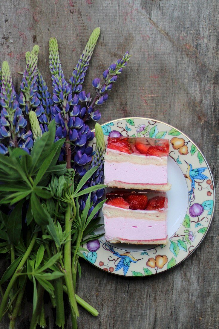 Two slices of strawberry cake on a plate next to lupin flowers