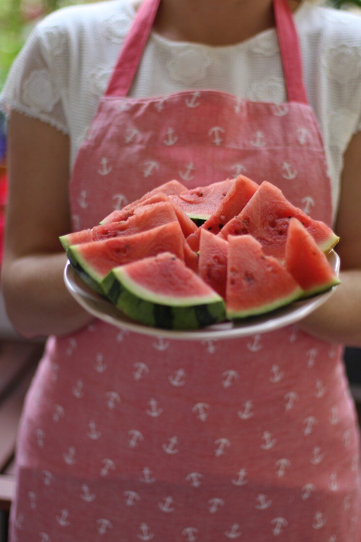 Frau mit Schürze hält Teller mit Melonenstücken