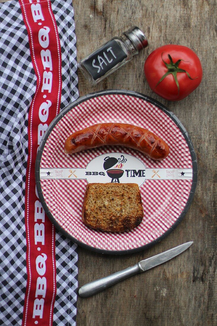 Grilled sausage and a slice of bread on a paper plate (seen from above)