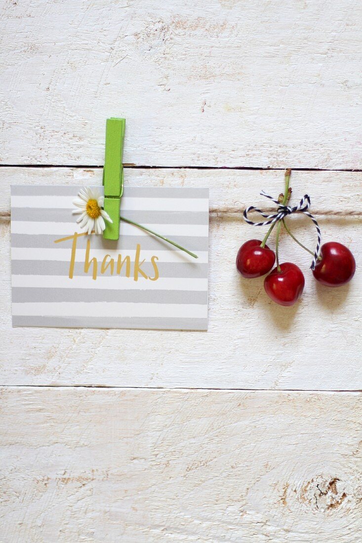 A thank you card and three red cherries hanging on a line