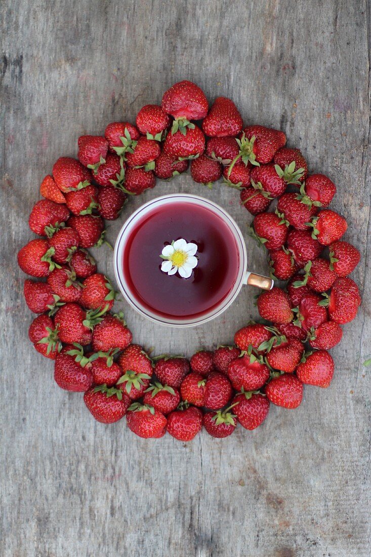 A cup of strawberry tea surrounded by fresh strawberries (seen from above)