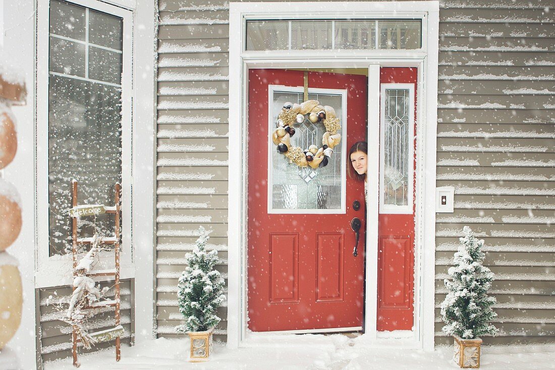 Woman peeping out of open front door on snowy day