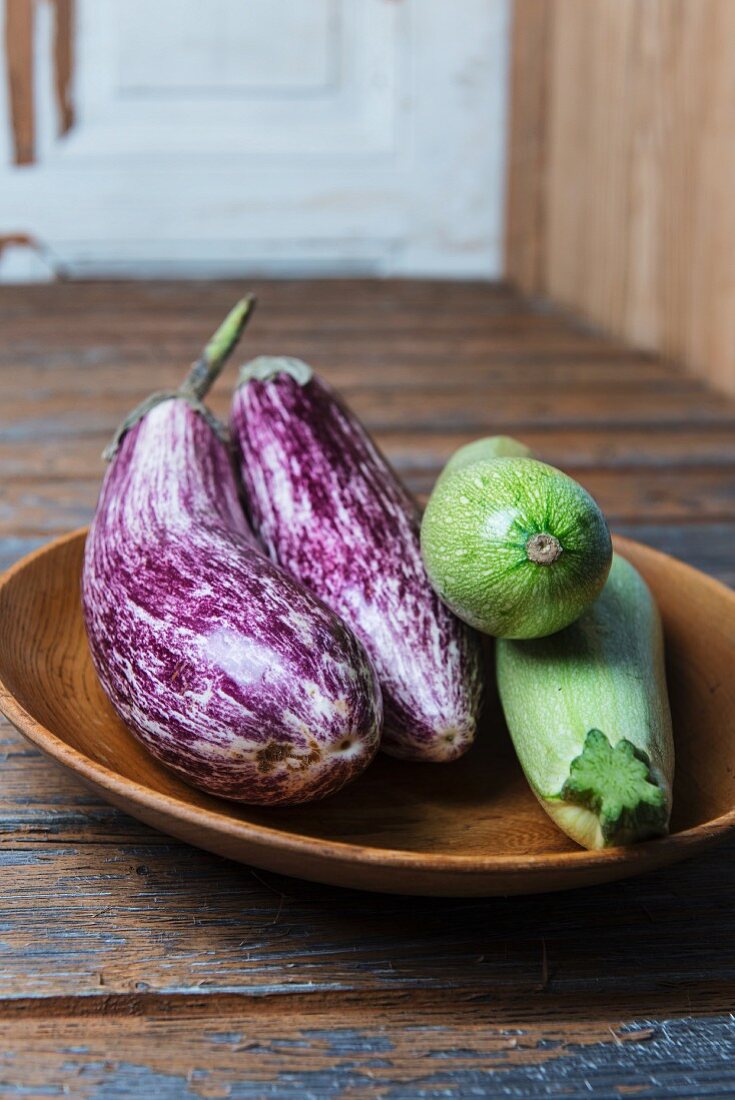 Aubergines and courgettes in a wooden bowl on a wooden surface