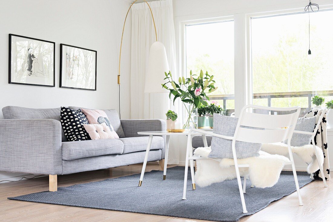 Pale grey couch, designer standard lamp and sheepskin on white garden chair in front of window in lounge area