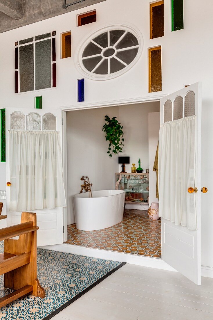 Kunsthandwerkliche Wandgestaltung mit Buntglas und Blick in Bad mit freistehender, weisser Badewanne