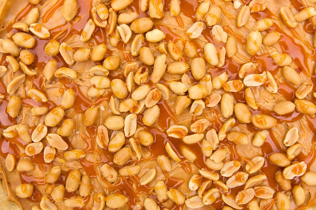 Caramel sauce being poured over peanuts on peanut butter