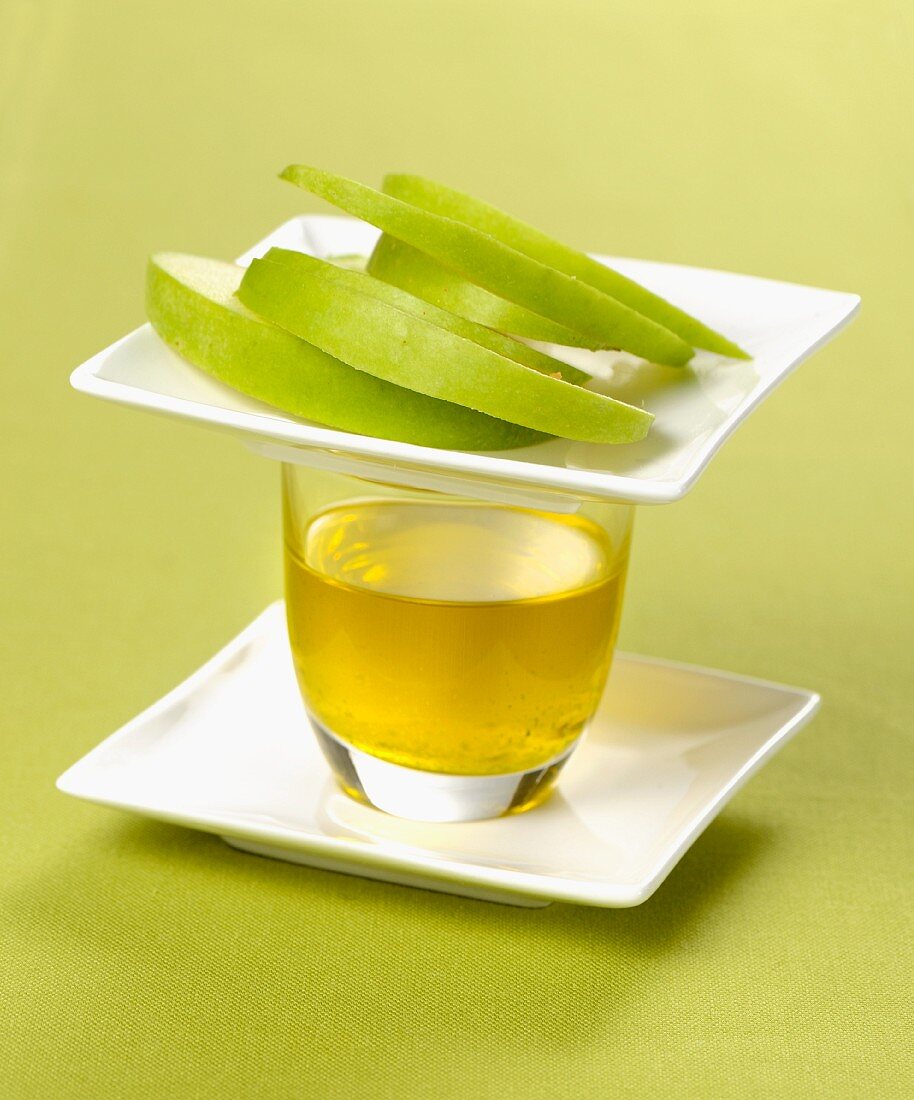 A glass of olive oil and sliced green apple