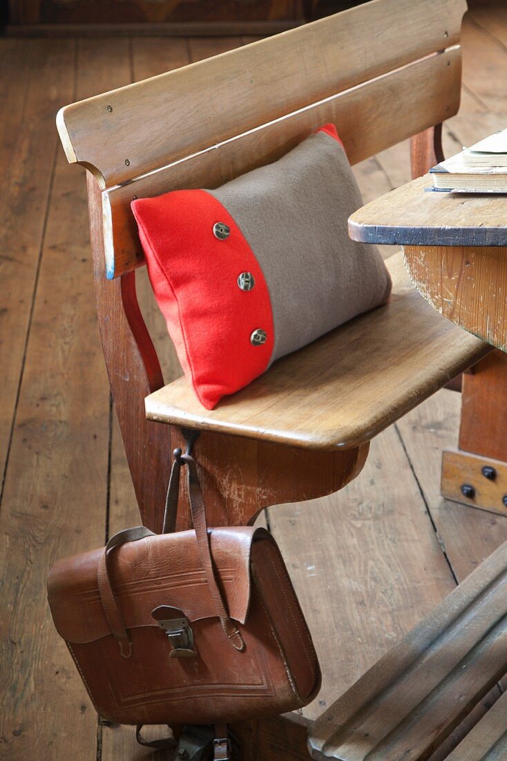 Scatter cushion with two-tone boiled-wool cover on vintage school bench with old-fashioned leather satchel hanging from backrest