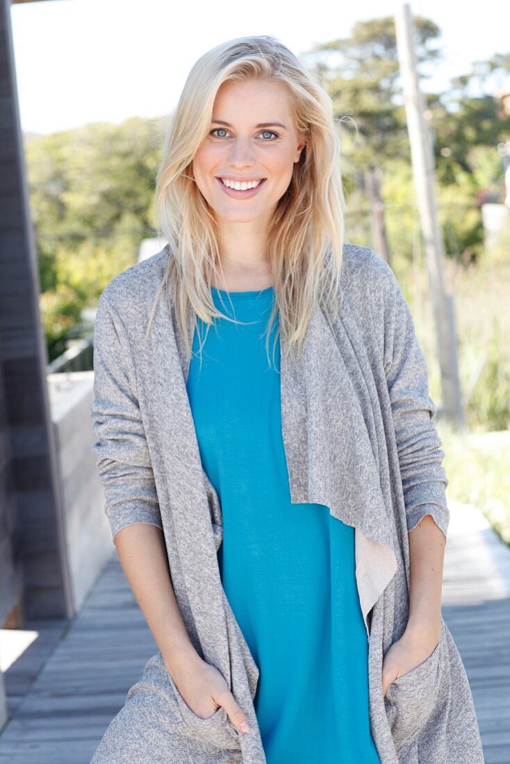 A young blonde woman wearing a blue top and a grey shirt coat