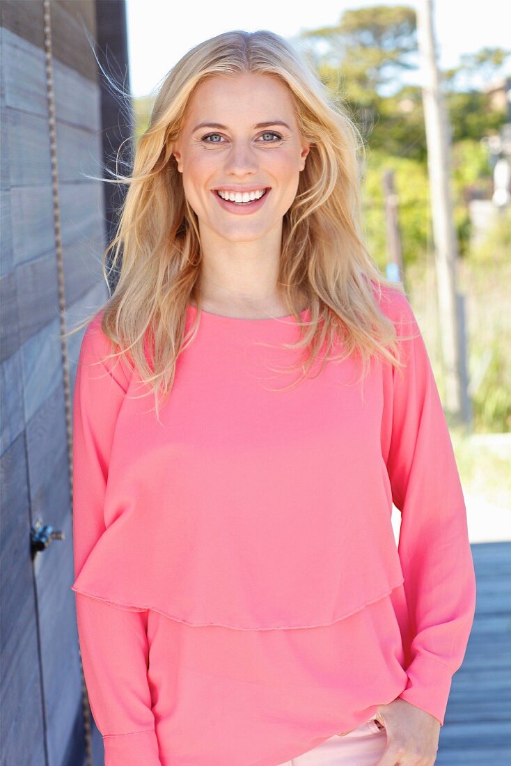 A young blonde woman wearing a long-sleeved, layer-look top and pink trousers