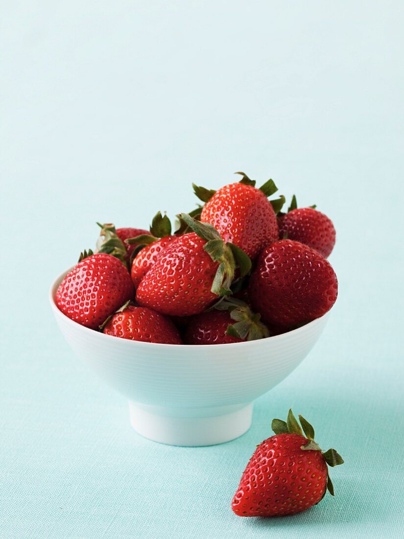 A bowl of strawberries with one next to it
