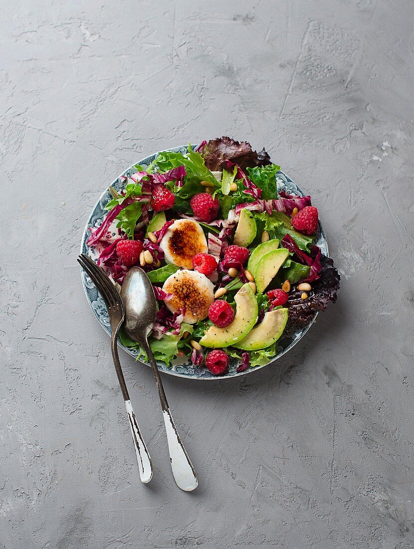 A mixed leaf salad with avocado, raspberries, goat's cheese and pine nuts