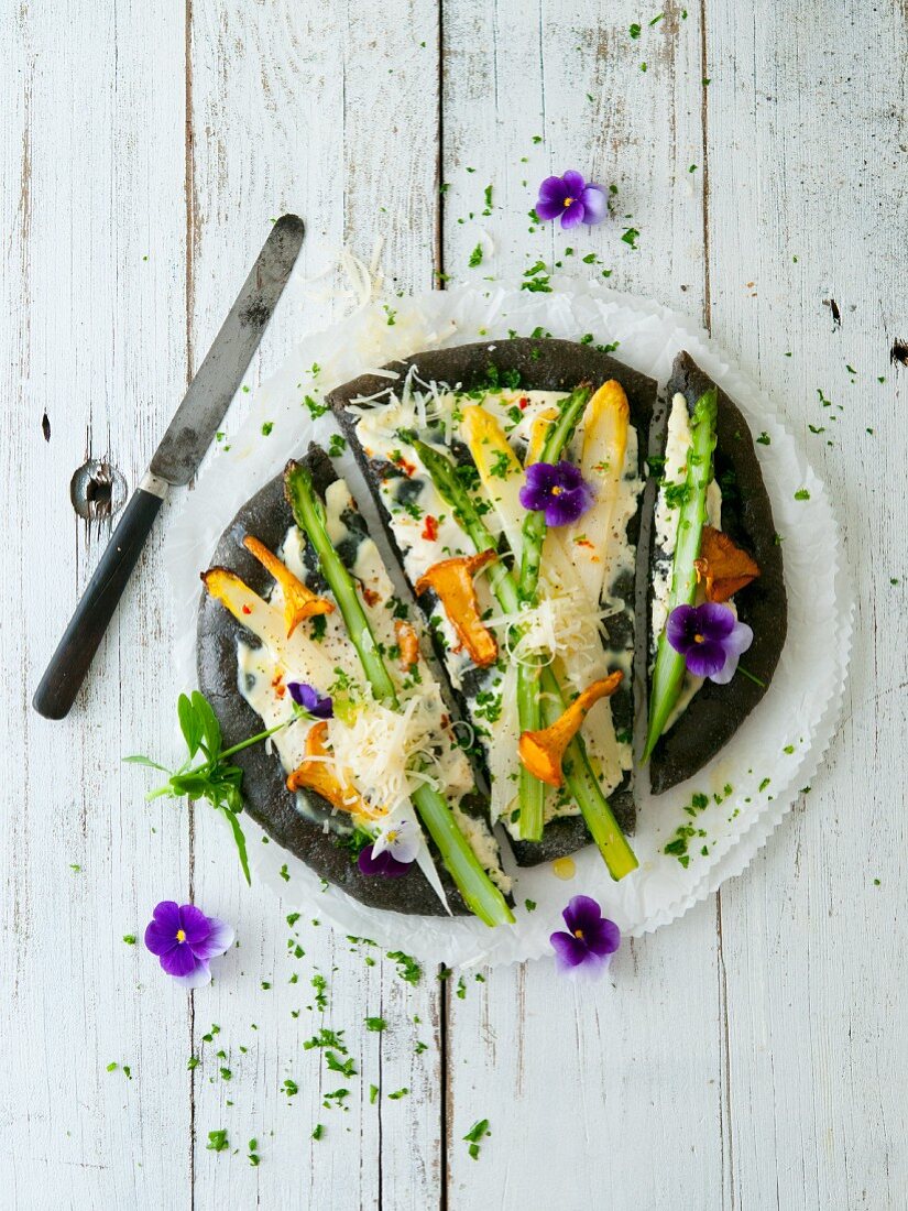 A black pizza with asparagus and chanterelle mushrooms