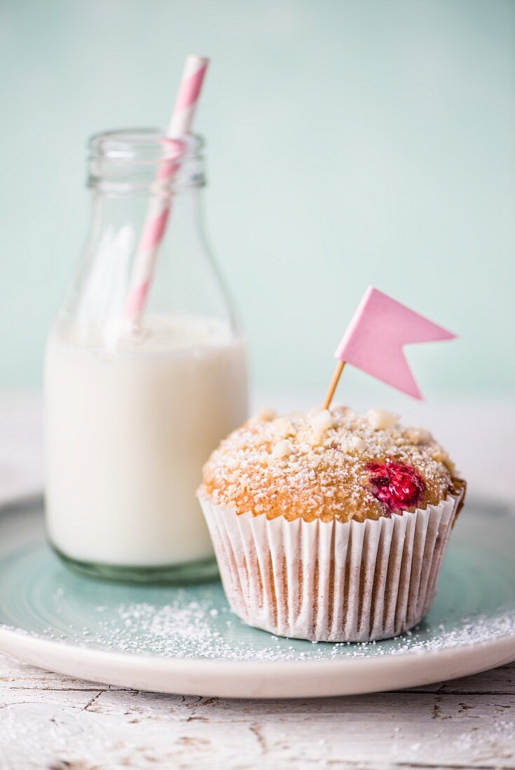 A raspberry muffin with white chocolate next to a small bottle of milk with a straw