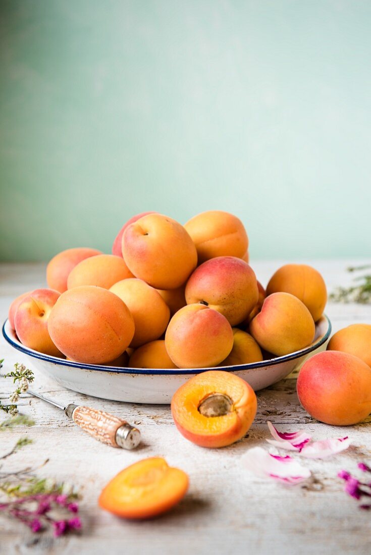 Fresh apricots in an enamel bowl next to a knife