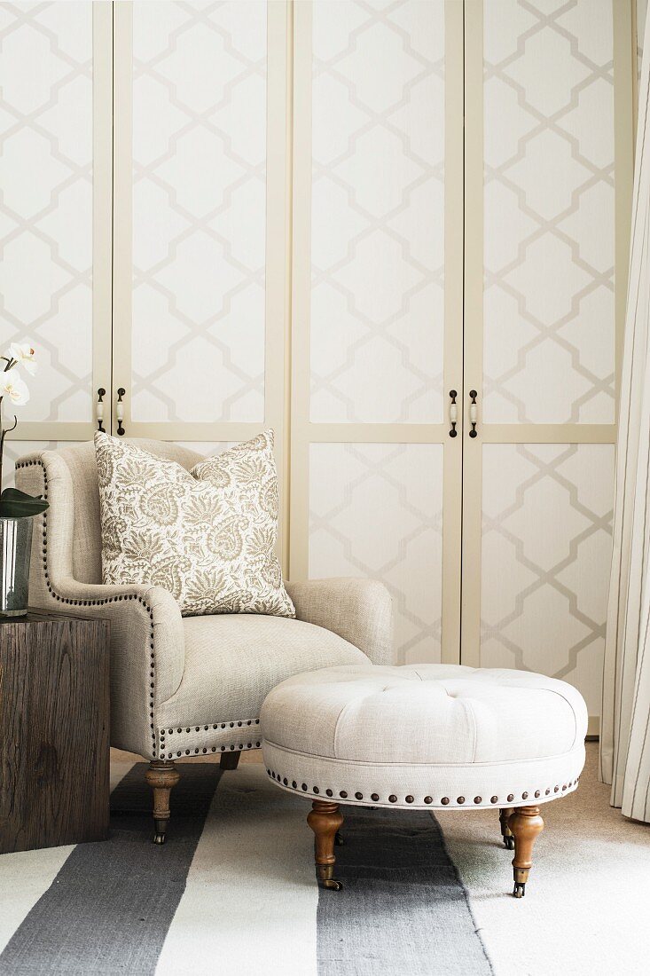 Armchair and footstool in front of cupboards with wallpapered doors