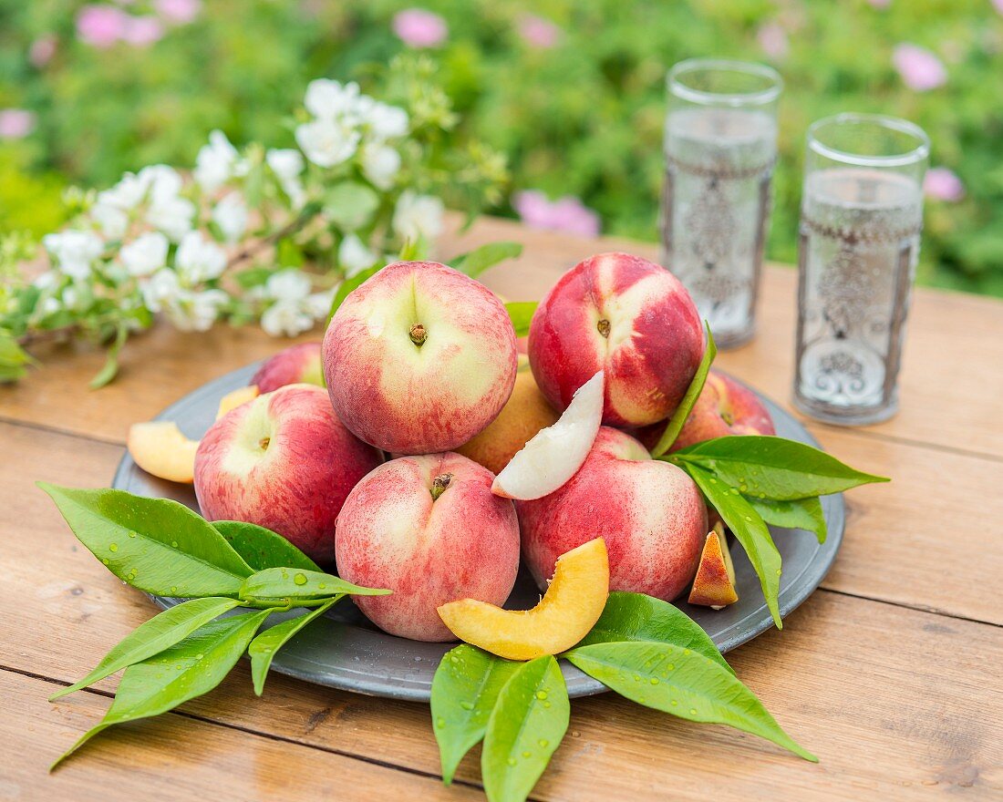 Peaches with leaves on a plate on a garden table
