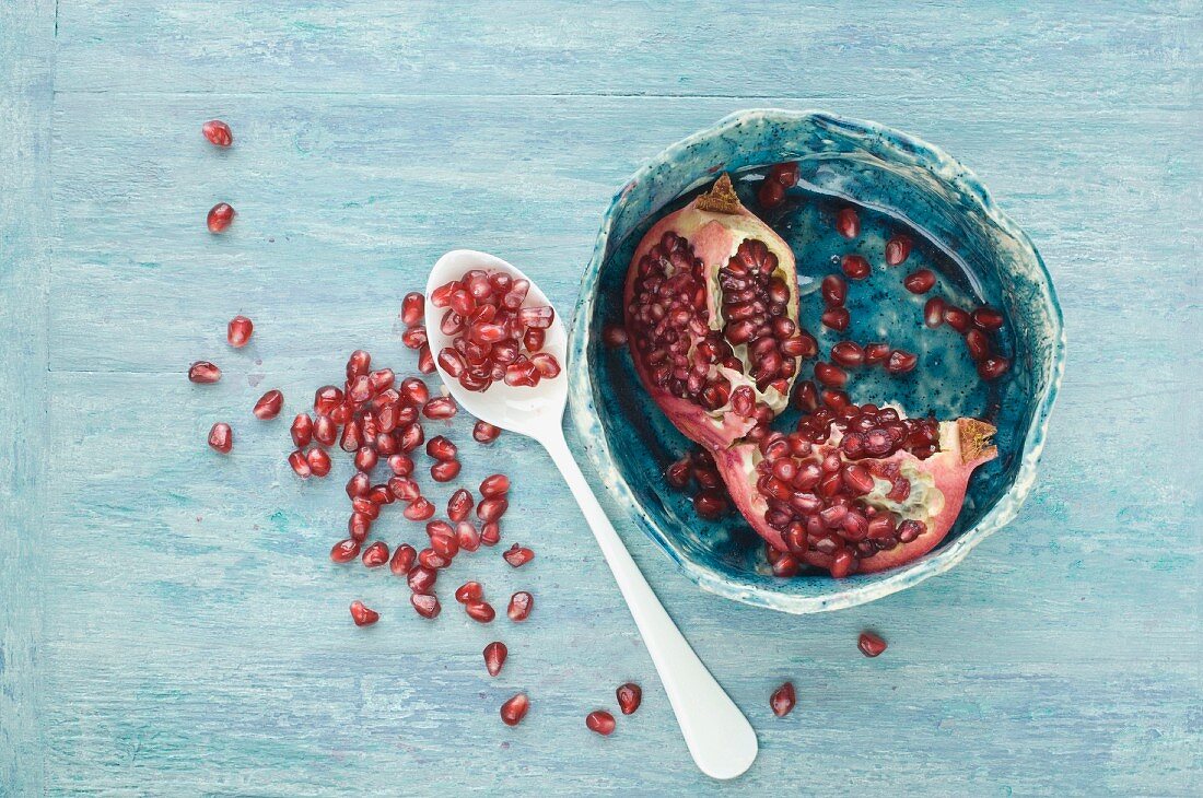 A bowl of pomegranate seeds and a piece of pomegranate on a wooden surface
