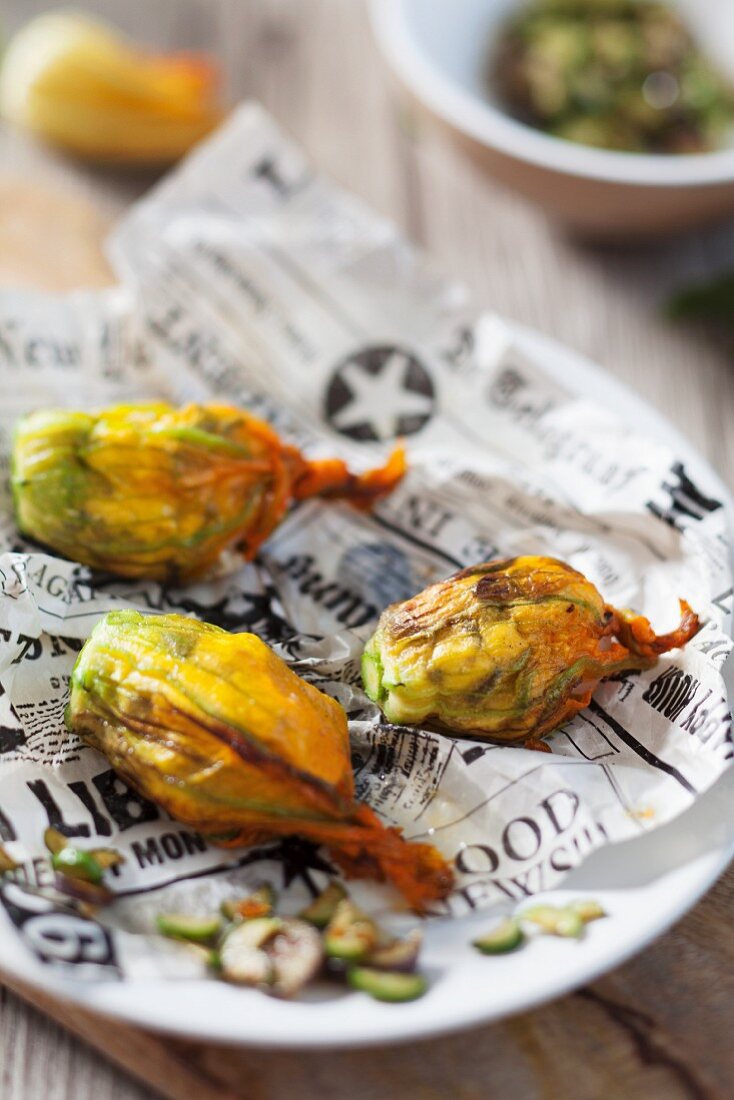 Stuffed courgette flowers on a piece of newspaper on a plate