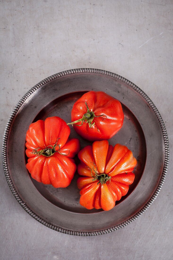 Three beefsteak tomatoes on a metal plate (seen from above)