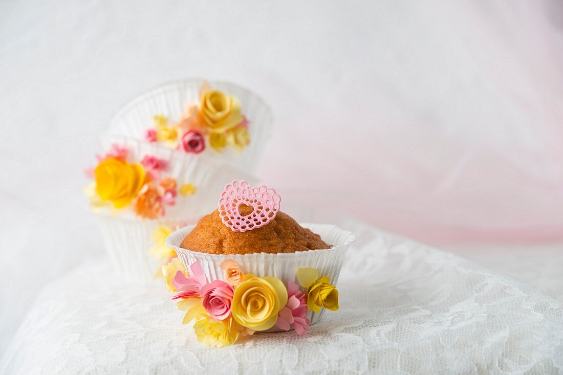 Cupcake mit Zuckerherz in Förmchen dekoriert mit Papierblüten