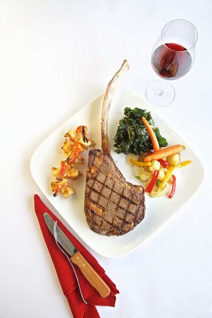 Grilled tomahawk steak with side dishes and a glass of red wine (seen from above)