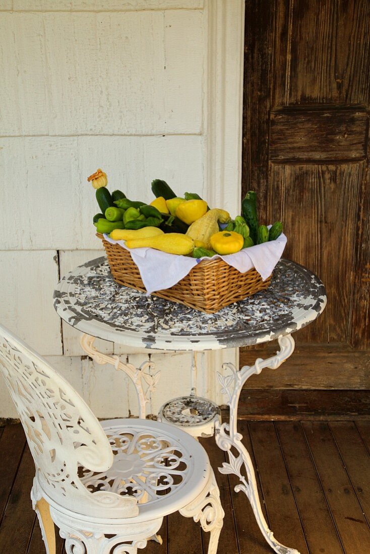 Korb mit frischen Kürbissen und Zucchini auf antik-weißem Terrassentisch