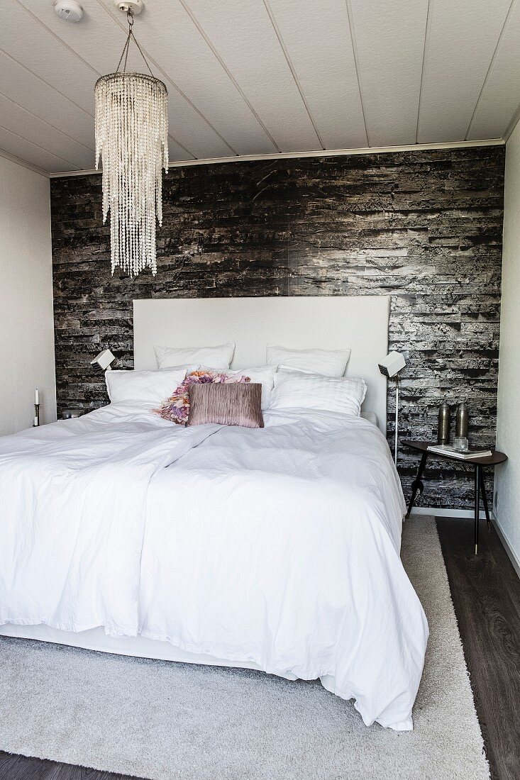 Double bed and chandelier in bedroom with dark wallpaper