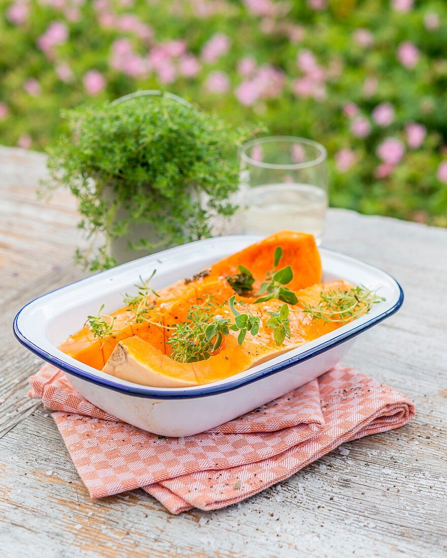 Quartered butternut squash with oil and herbs in a baking dish