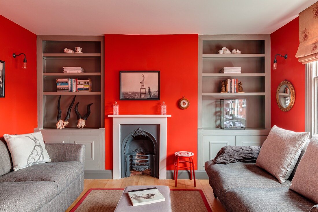 Red walls, grey fitted shelving and vintage fireplace in living room