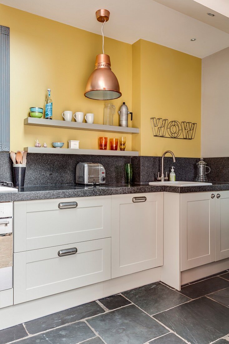 Kitchen counter with granite worksurface below two grey shelves mounted on yellow wall