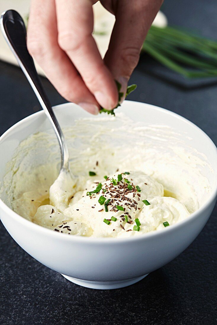 Quark and flaxseed oil spread being sprinkled with herbs