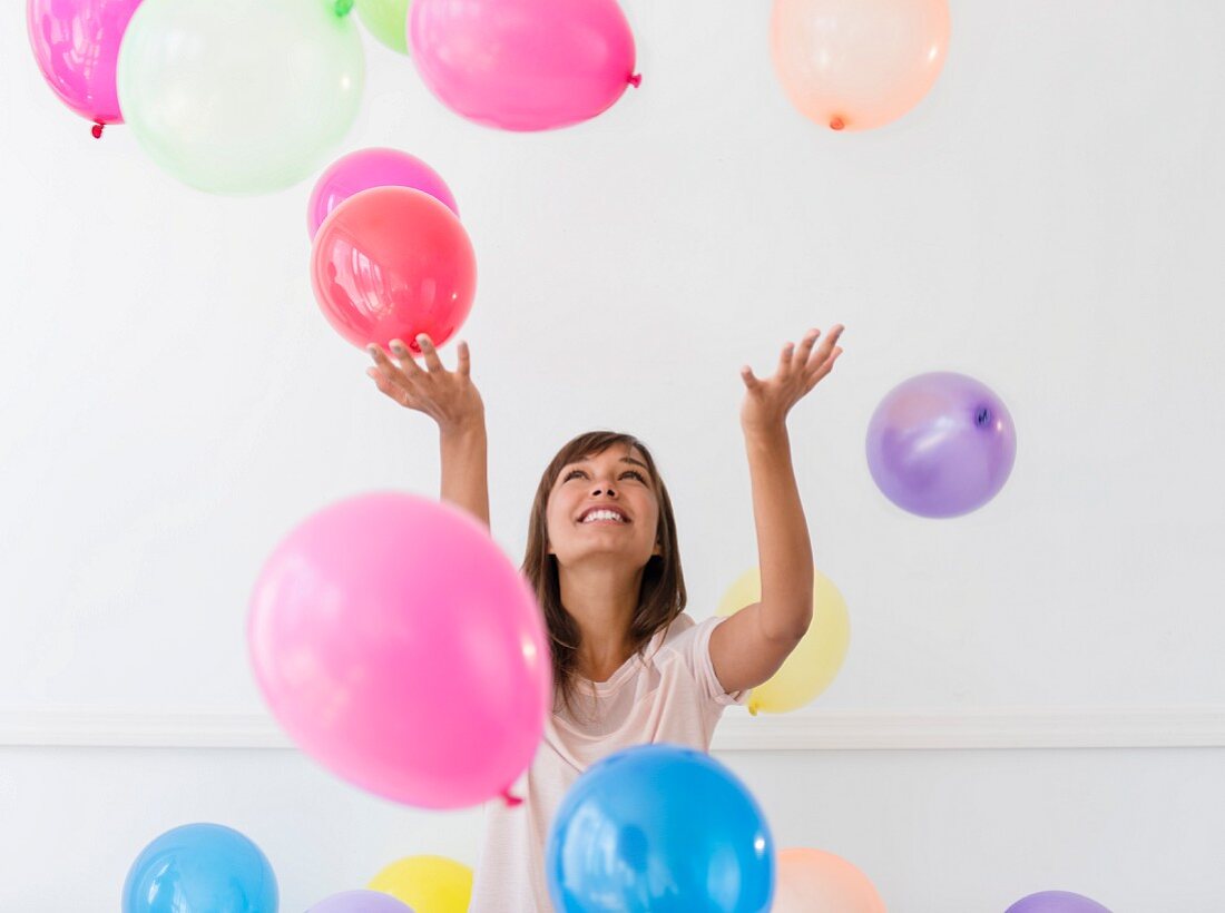 A young brunette woman playing with colourful balloons