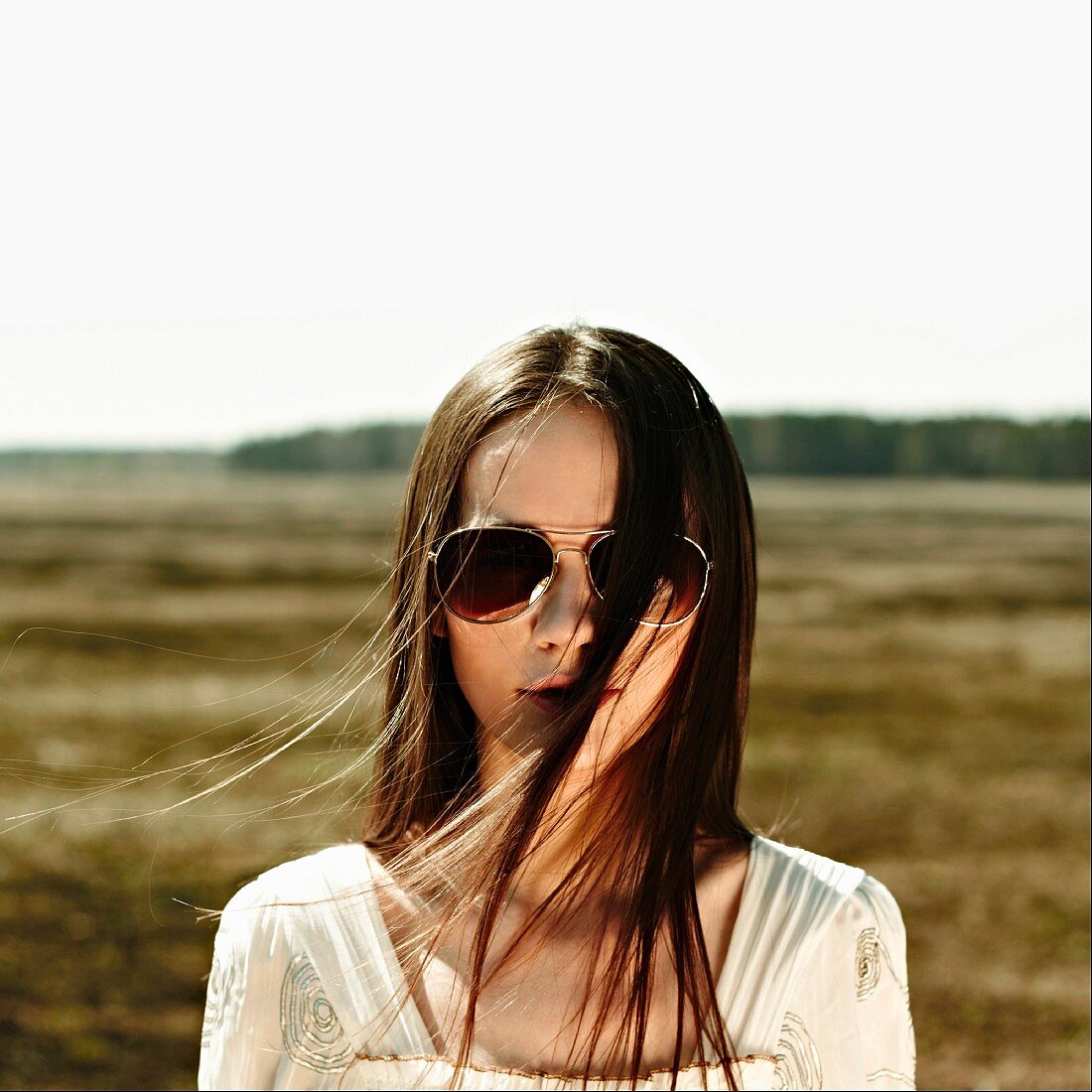 A young brunette woman wearing a pair of Pilot sunglasses standing in a field