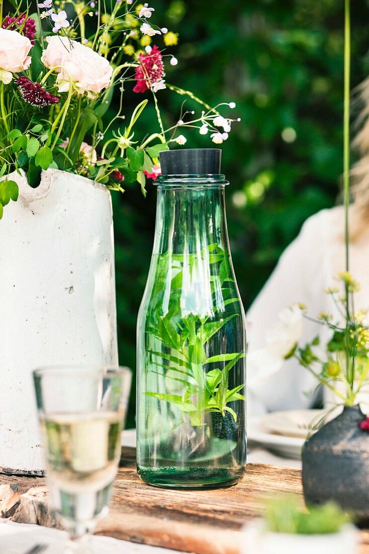 Mineralwasser mit frischen Kräutern in Glaskaraffe auf Gartentisch