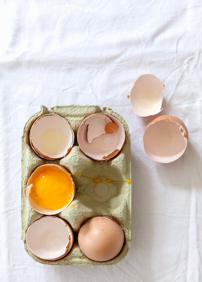 A whole egg, empty eggshells and a cracked-open egg in an egg box