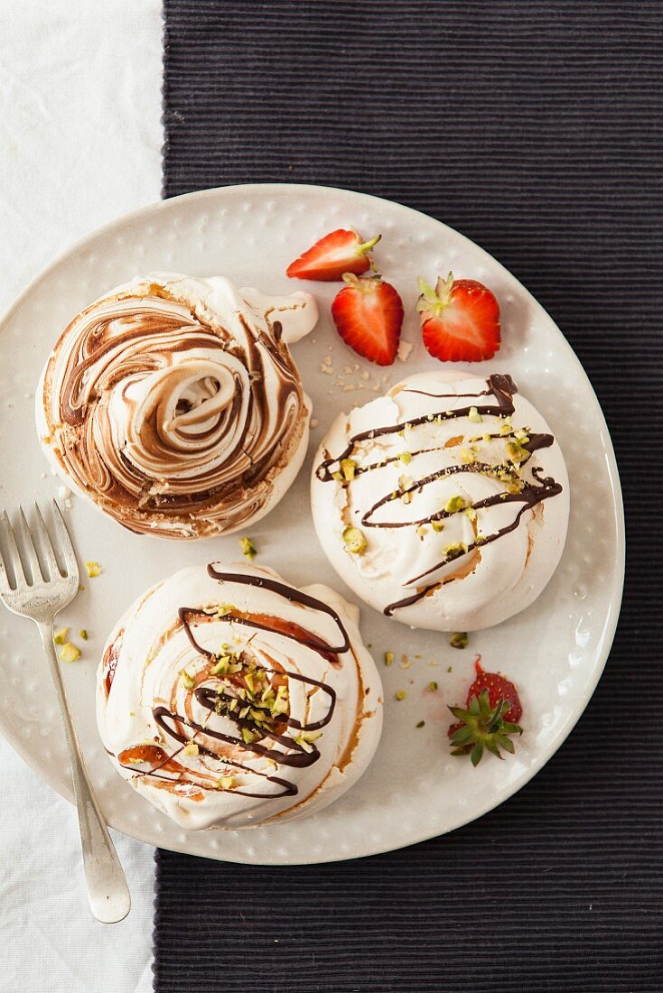 Various meringues with chocolate sauce, strawberries and pistachio nuts on a plate