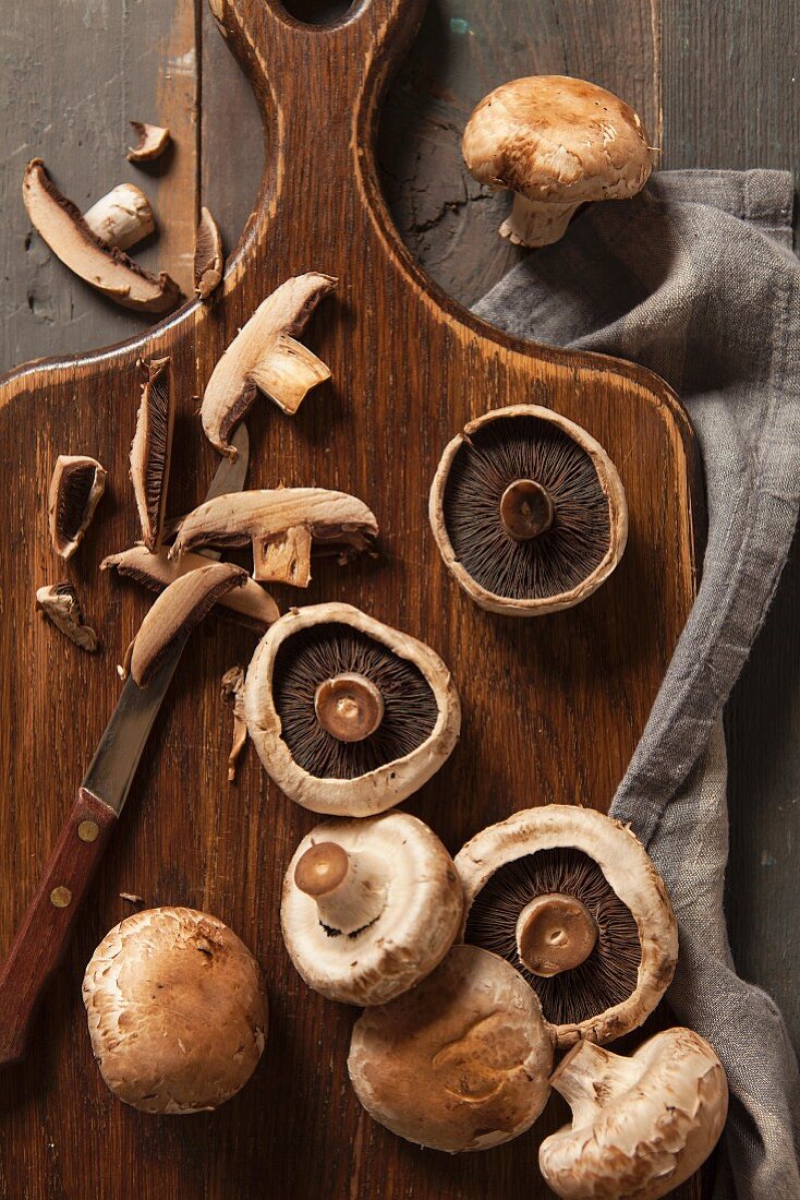 Frische Pilze, teilweise geschnitten, mit Retro-Messer auf Holzschneidebrett