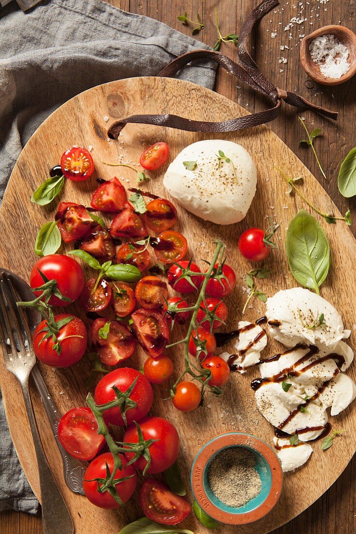 Gemischte Tomaten mit Mozzarella und Basilikum, schwarzer Pfeffer, Thymian und Balsamico auf Holzplatte