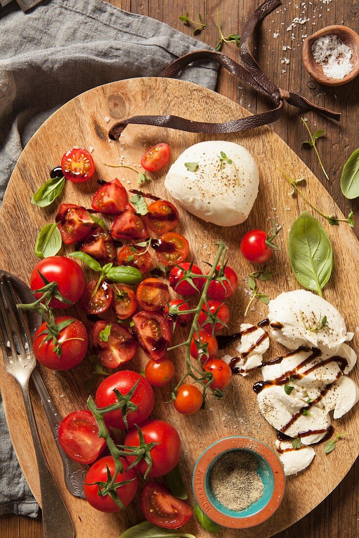 Mixed tomatoes with mozzarella and basil, black pepper, thyme and both balsamic sauce on a wooden board