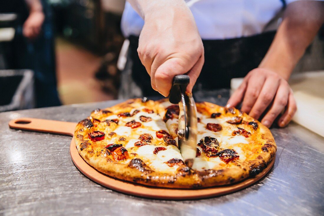 Koch schneidet Pizza mit Pizzamesser in Restaurantküche