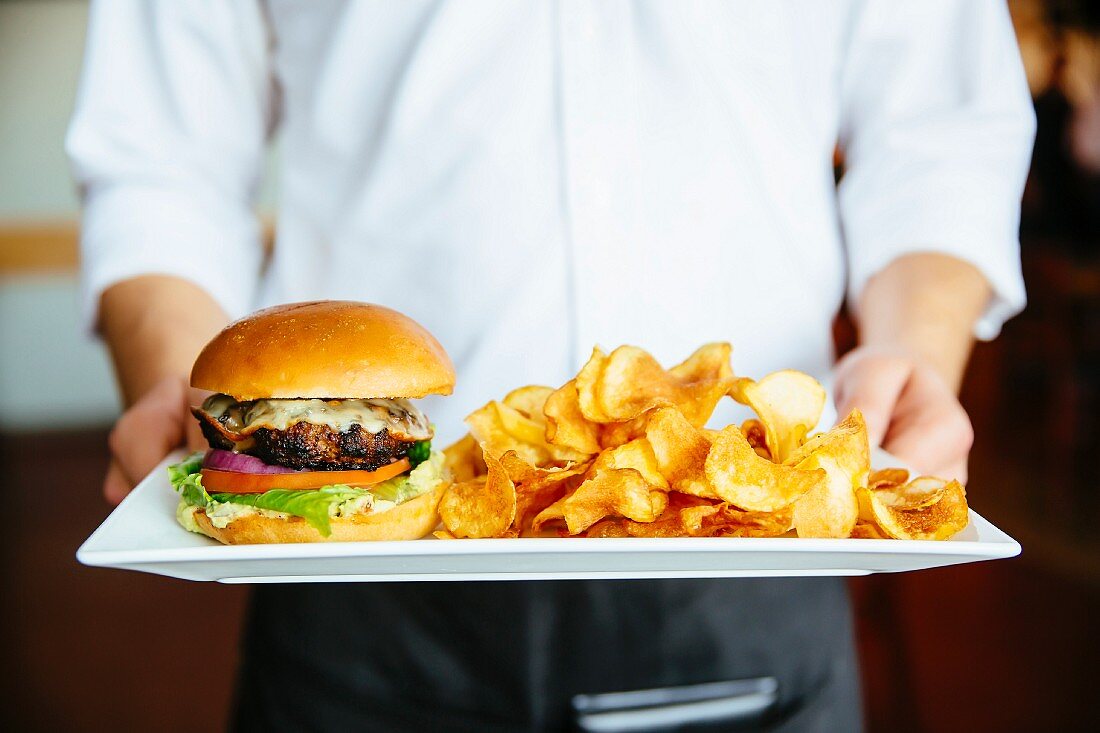A waiter serving a cheeseburger and chips on a tray