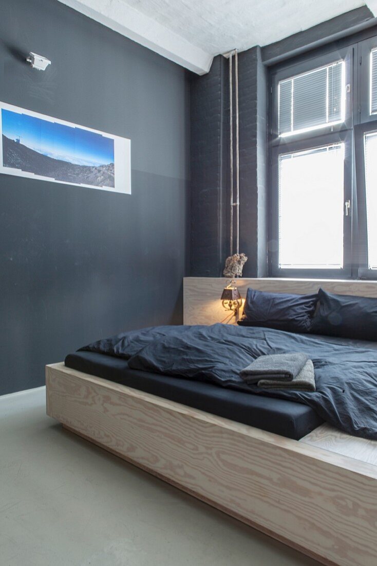 Modern wooden bed and photo art on black wall in minimalist bedroom